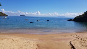 A beach with calm waters, boats, and a clear sky. - Coronado Beach (Búzios)