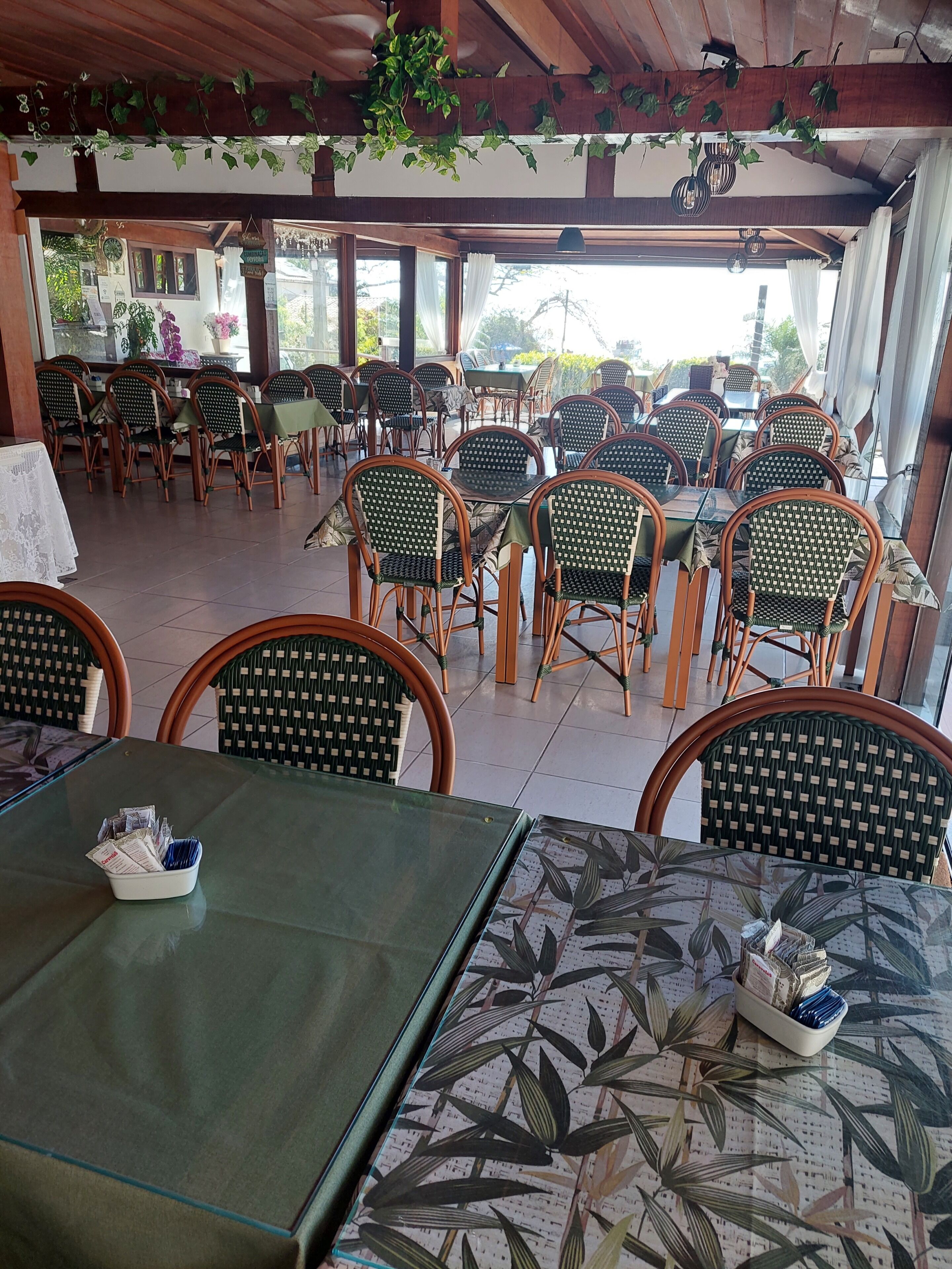 A restaurant with outdoor seating, wicker chairs, and tables with green and patterned tablecloths.
