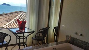 A bathroom with a large bathtub, a glass table with chairs, and a view of the sea through a window. - Coronado Beach (Búzios)