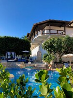 Area piscina con sedie a sdraio e ombrelloni, un muro in pietra e un edificio con un balcone.