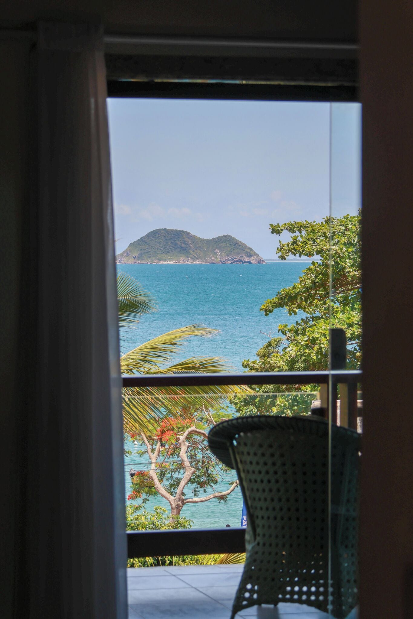 A view from a balcony with a clear blue sea, a distant island, and a chair.