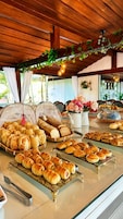 A buffet with various baked goods, including bread and pastries, under a wooden ceiling with hanging lights.