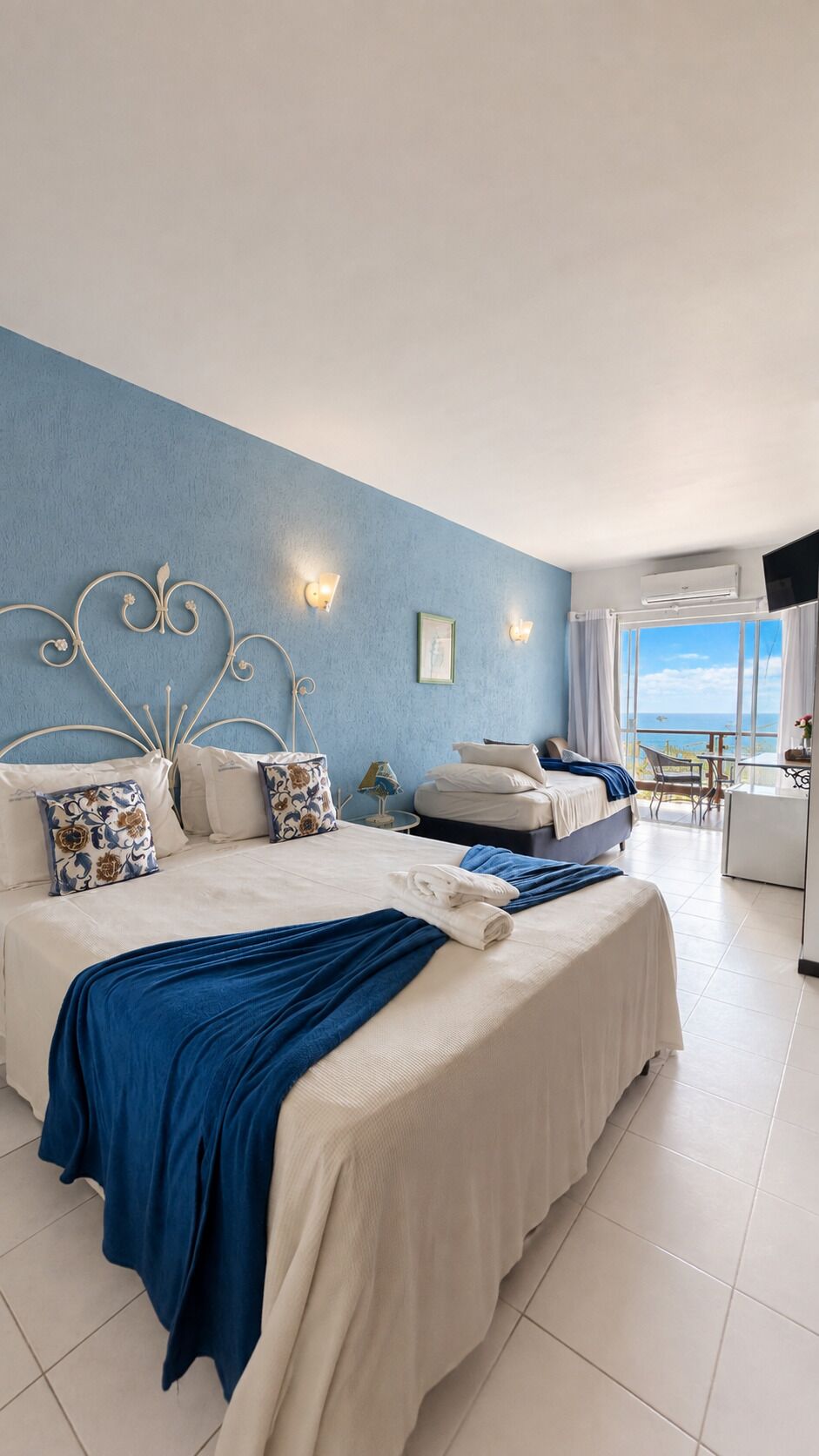 Quarto de hotel com duas camas, uma janela grande e vista para o mar.