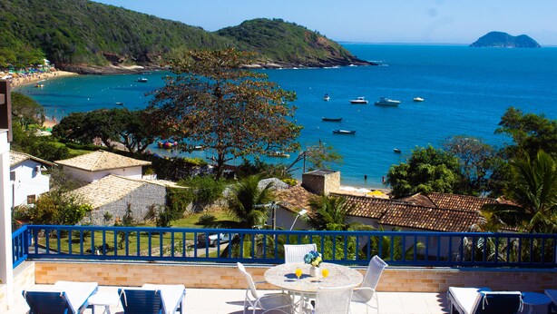 A seaside terrace with white tables and chairs, overlooking a beach with boats and a clear view of the sea. - Coronado Beach (Búzios)