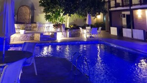 A nighttime pool area with lounge chairs and a small pool, surrounded by a building with a bell tower and a covered patio. - Coronado Beach (Búzios)