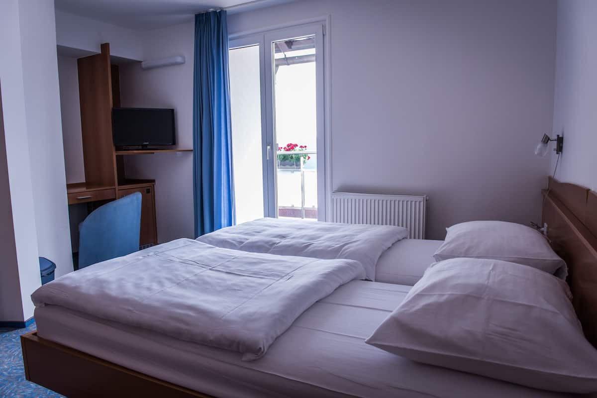 Una habitación de hotel con cama, televisor sobre un mueble, ventana con cortinas y radiador.