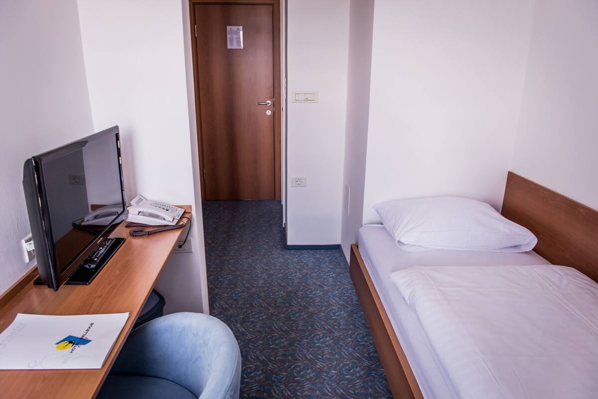 Una habitación de hotel con escritorio, computadora, teléfono, cama y puerta que da a otra habitación.