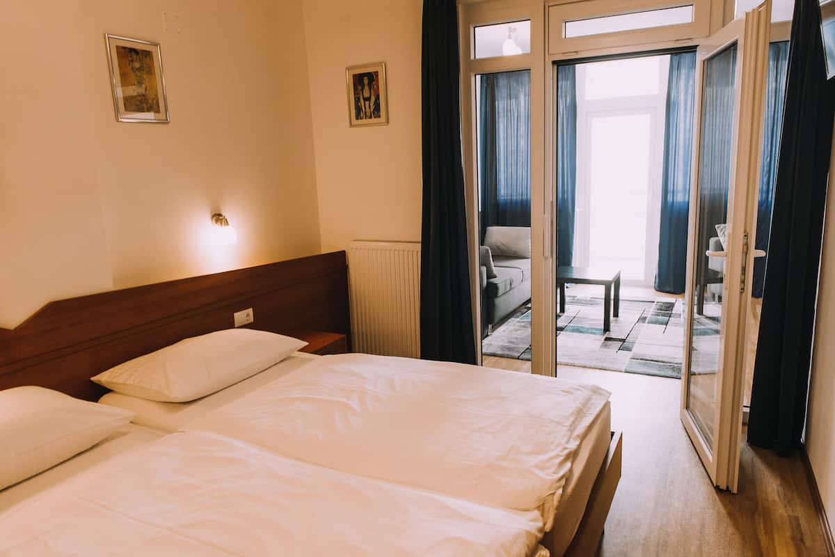 Habitación de hotel con dos camas, cabecero de madera, una mesita y vistas a un balcón a través de un ventanal.