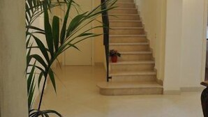 A hallway with a staircase leading to a room. There are potted plants and wall sconces. - Il Mattino ha l'oro in bocca (Pisa)
