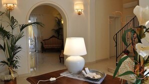 A well-lit lobby with a large white lamp, a wooden table with a tray, and a staircase. - Il Mattino ha l'oro in bocca (Pisa)