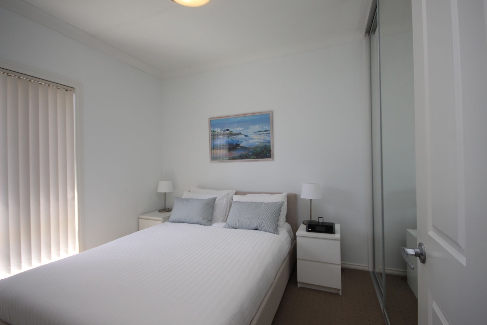 A bedroom with a bed, two bedside tables, and a painting on the wall.