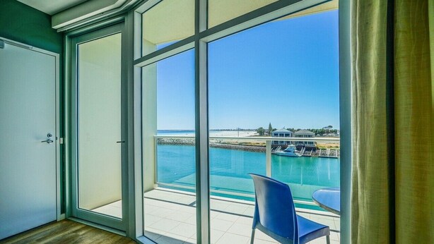 Een kamer met een grote schuifglazen deur die leidt naar een balkon met uitzicht op een strand en water.