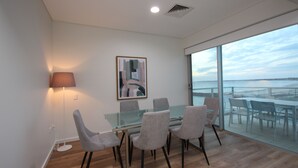 Een moderne vergaderruimte met een glazen tafel en stoelen, een vloerlamp en een groot raam met uitzicht op zee.