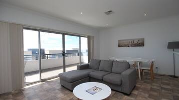 A modern living room with a grey sectional sofa, a round white coffee table, and a dining area with white chairs and a table.