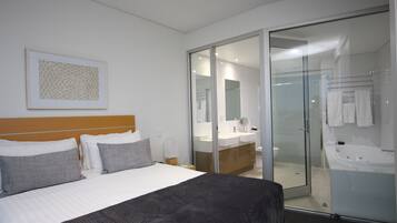 Una habitación de hotel moderna con una cama grande, una ducha con cerramiento de vidrio y un baño con bañera.