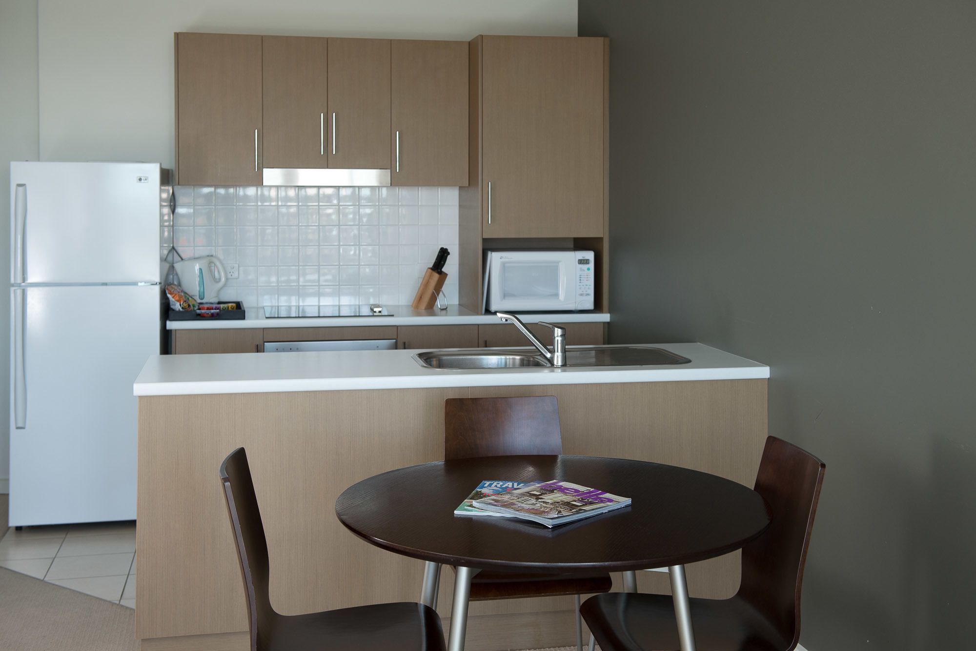 A compact kitchen with a refrigerator, microwave, sink, and a dining area with two chairs and a table.