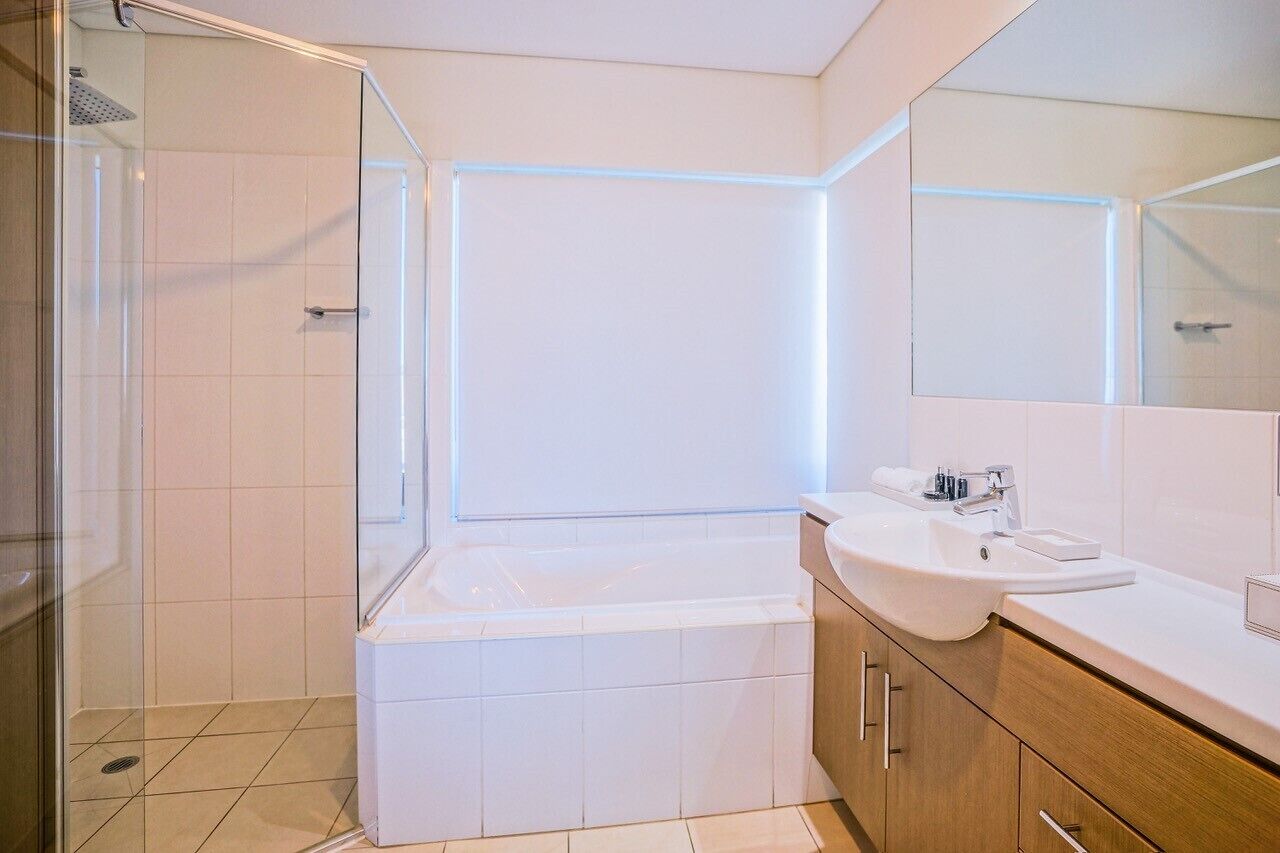 A modern bathroom with a glass-enclosed shower, a white bathtub, and a vanity with a sink and mirror.