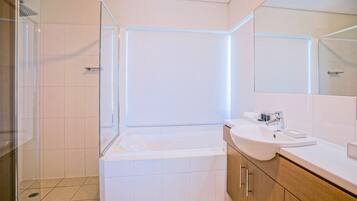 Ein modernes Badezimmer mit einer gläsernen Duschkabine, einer weißen Badewanne und einem Waschtisch mit Waschbecken und Spiegel.