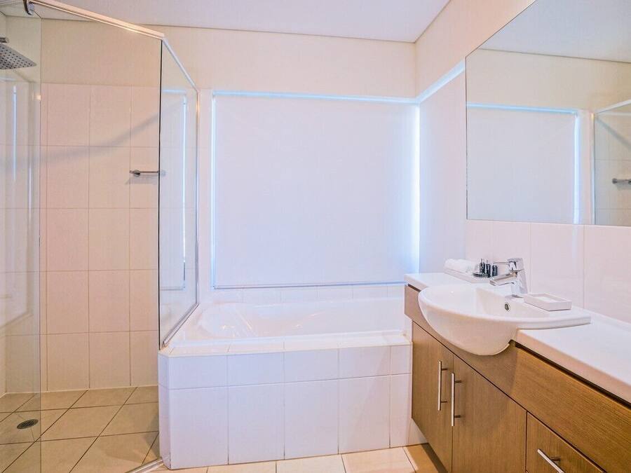 Ein modernes Badezimmer mit einer gläsernen Duschkabine, einer weißen Badewanne und einem Waschtisch mit Waschbecken und Spiegel.