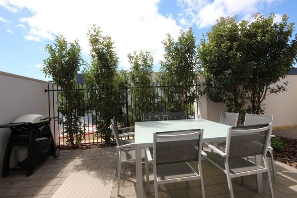 An outdoor patio with a table and chairs, surrounded by trees and a fence.