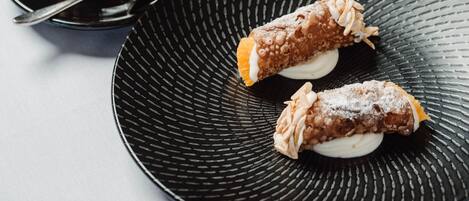 Une assiette noire avec deux cannolis et une tasse de café posée sur une soucoupe.