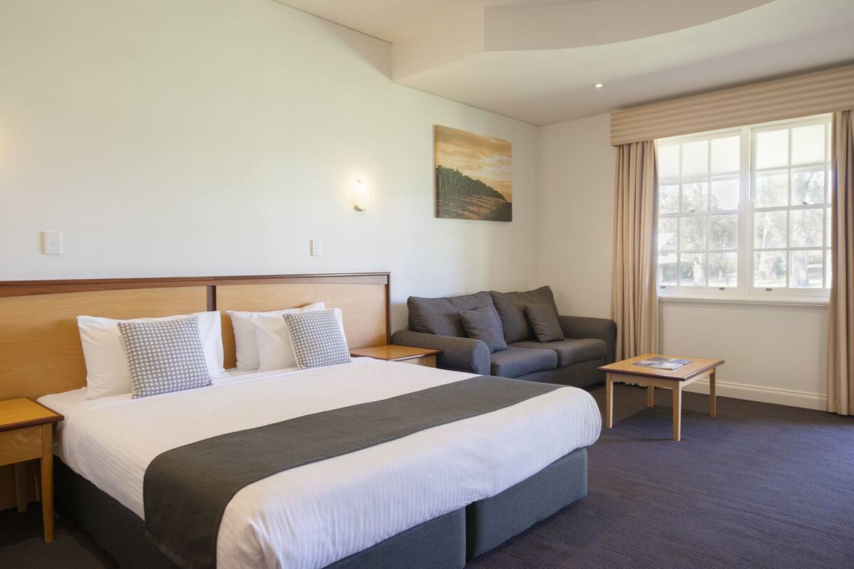 A hotel room with a large bed, a sofa, a small table, and a painting on the wall.