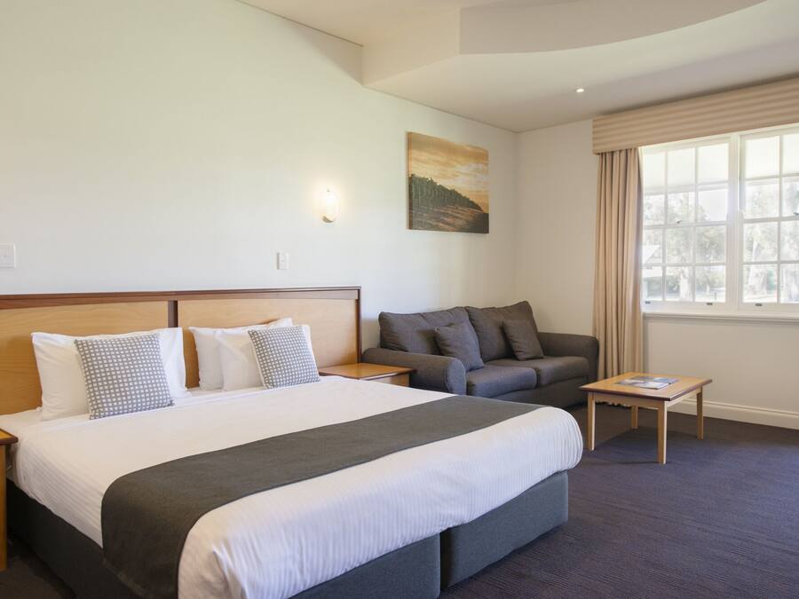 A hotel room with a large bed, a sofa, a small table, and a painting on the wall.