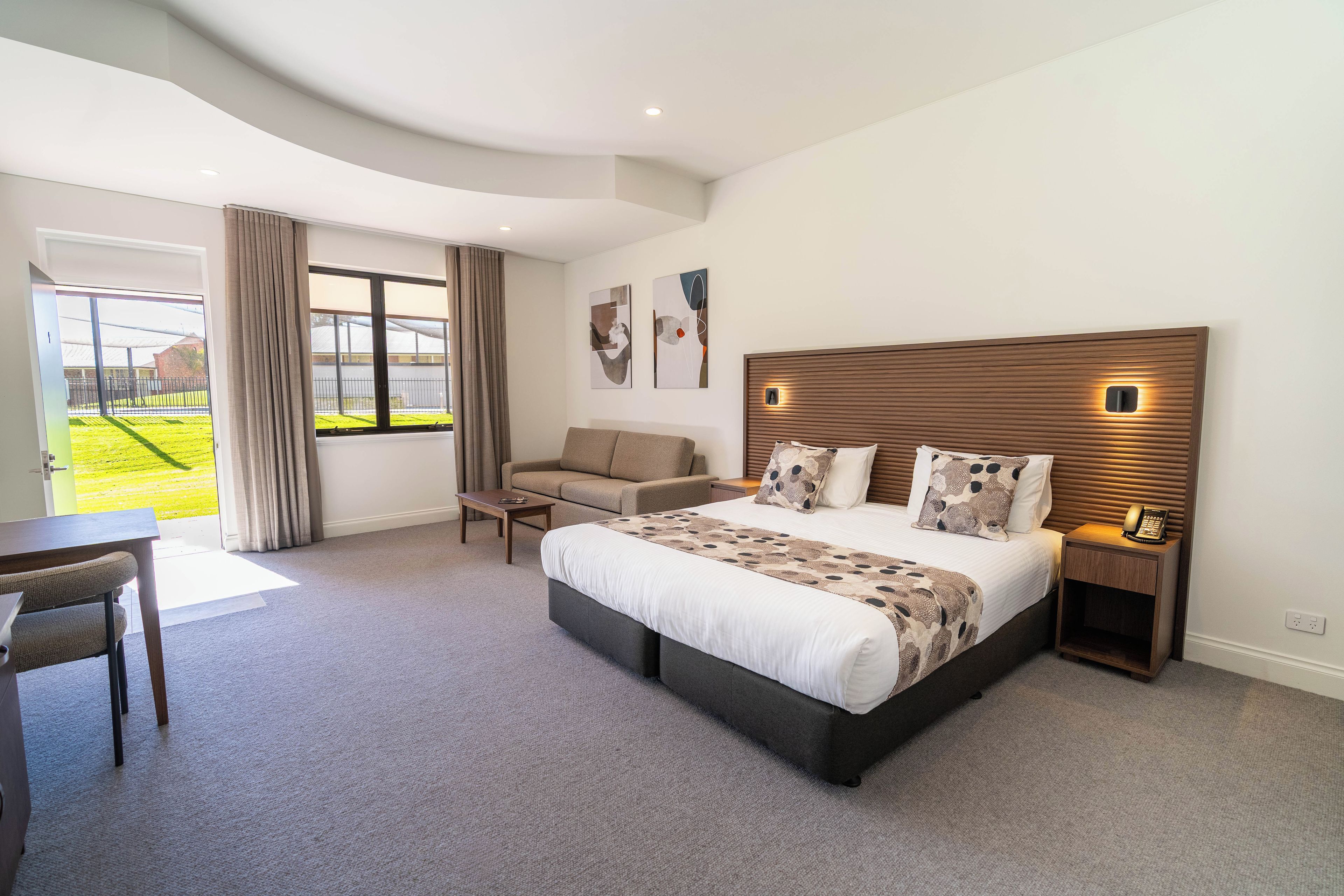 Habitación de hotel moderna con una cama grande, un sofá, un escritorio y vistas a un espacio exterior verde.