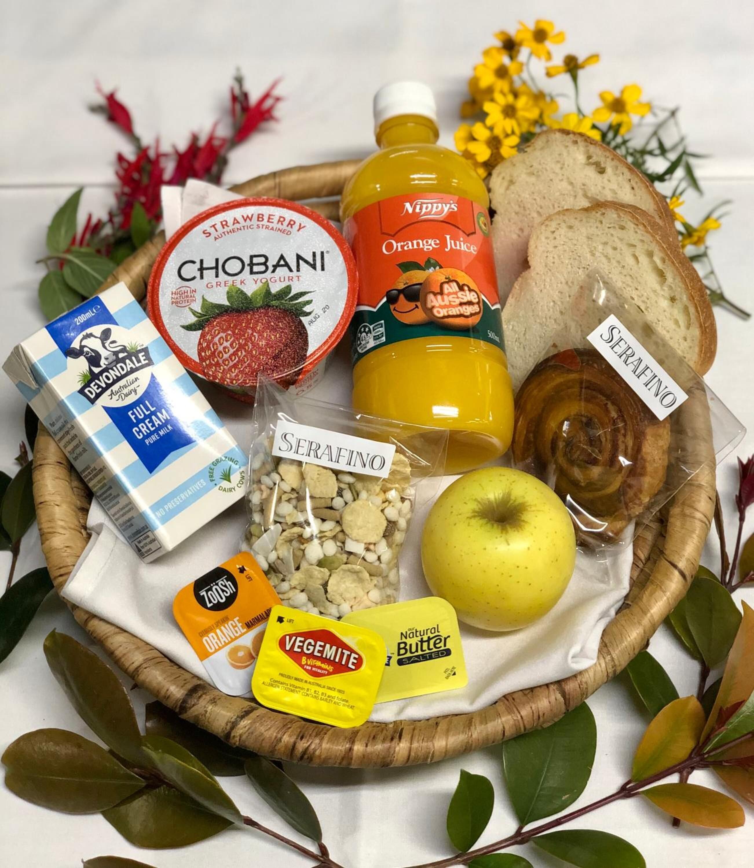 A variety of food items including Chobani Greek yogurt, orange juice, bread, and a bag of Serafino nuts, arranged on a table with a white cloth.