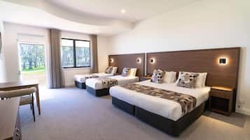 A modern hotel room with a large bed, two bedside tables, a desk, and a view of the outdoors.