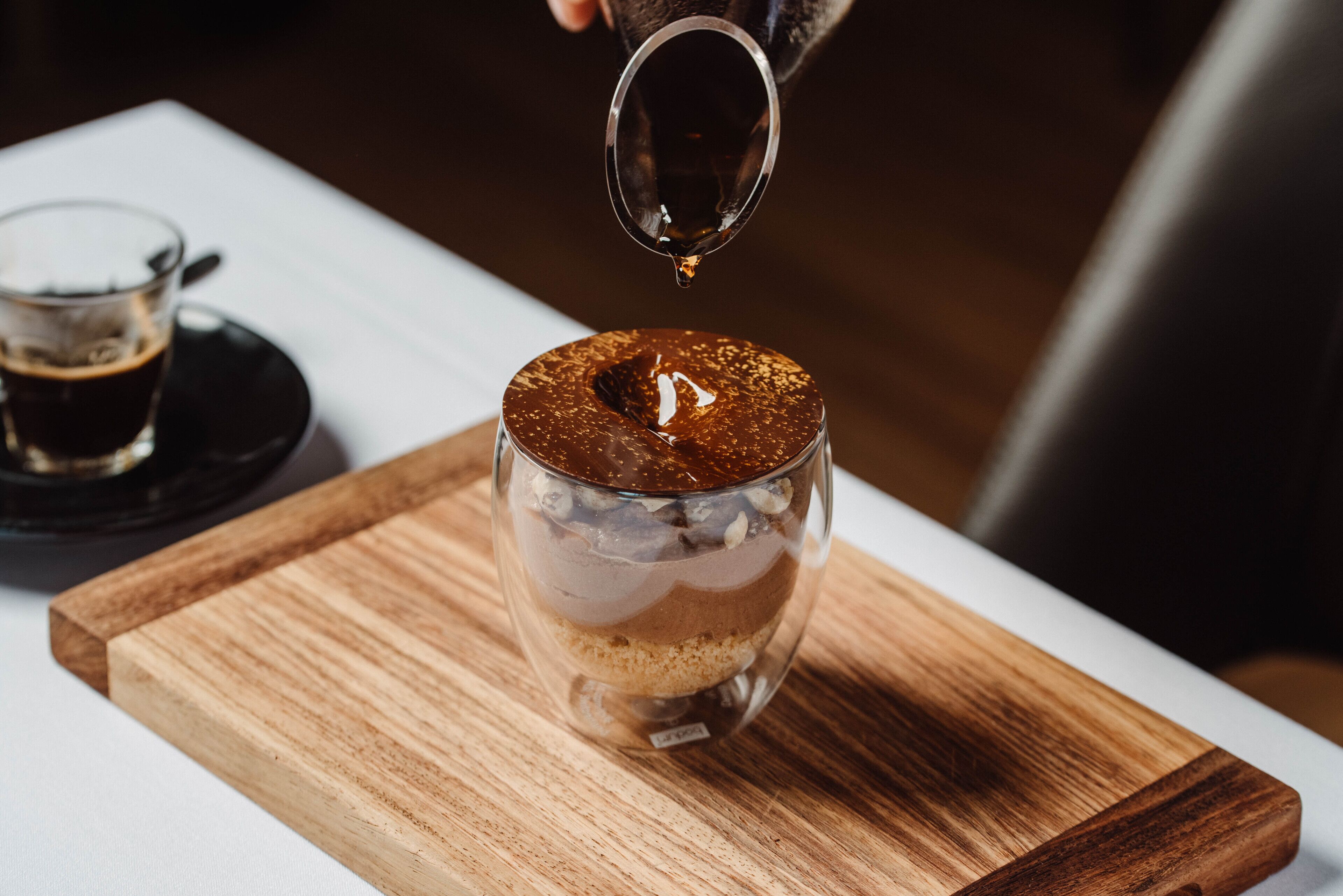 A layered dessert in a clear glass on a wooden board.