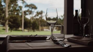 A dining table with a wine glass, a water glass, and a bottle of wine, set against a view of trees and a building.