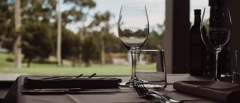 Una mesa de comedor con una copa de vino, un vaso de agua y una botella de vino, con vistas a árboles y un edificio.