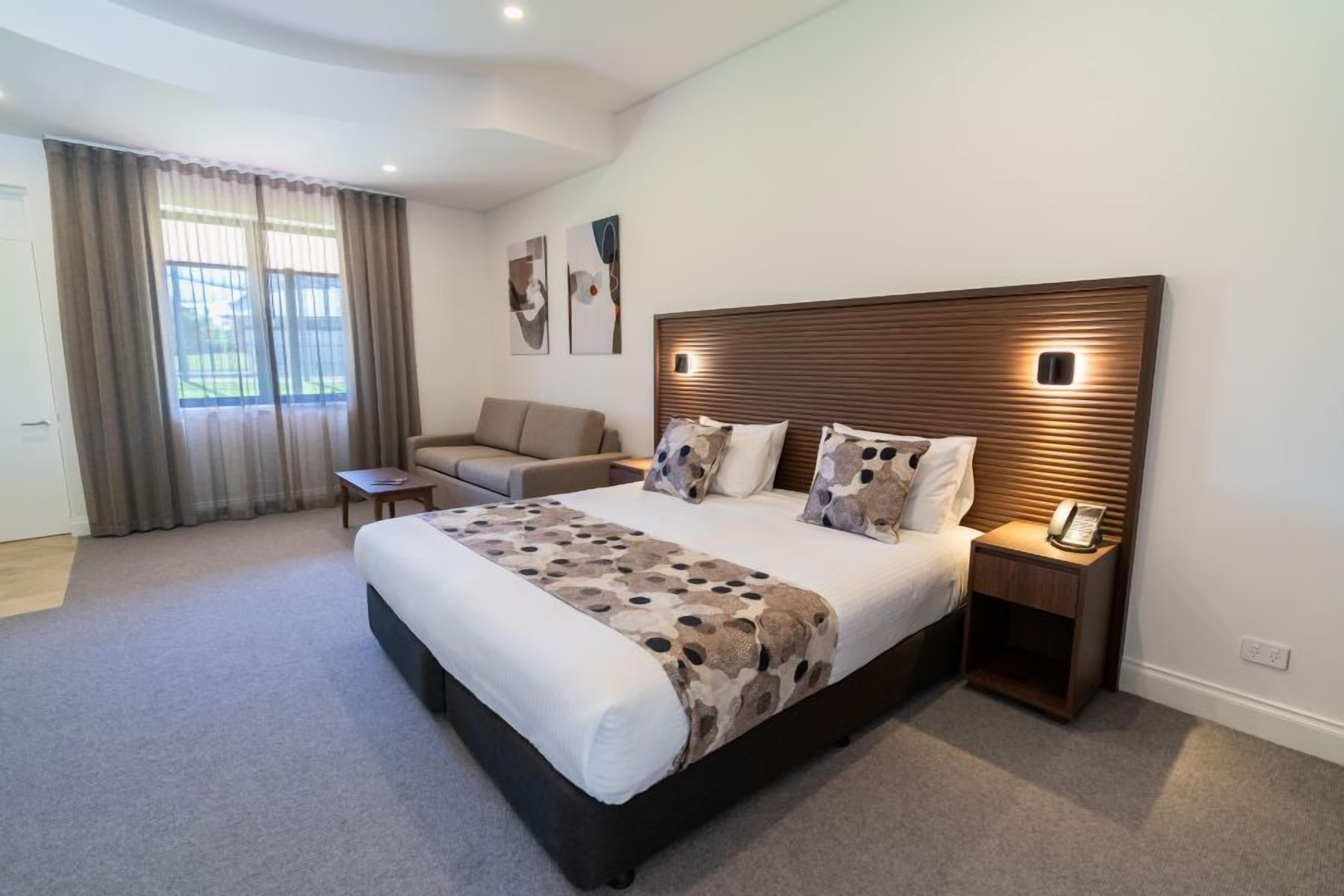 A modern bedroom with a large bed, bedside tables, a sofa, and a view of the outdoors.