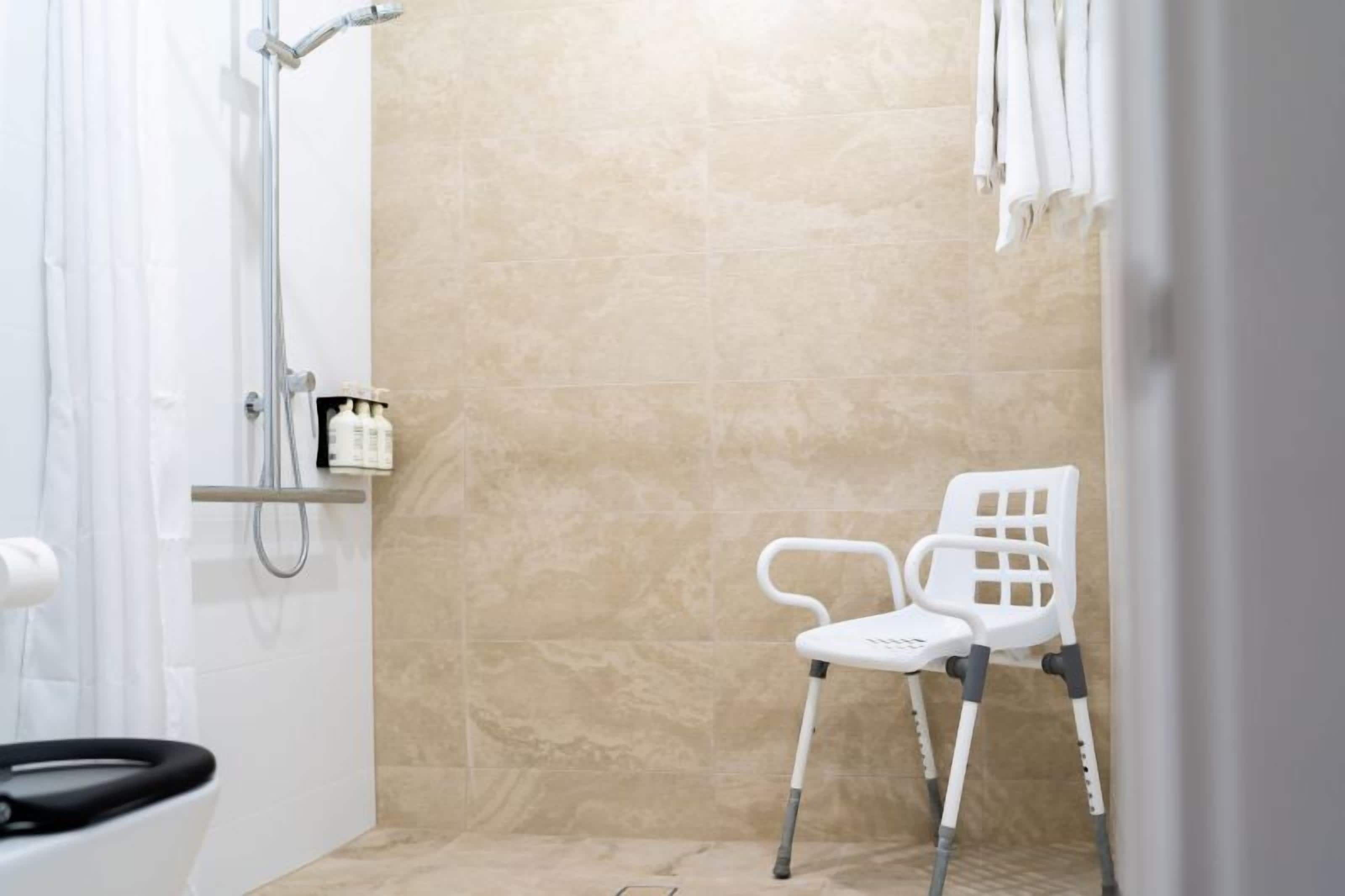 A bathroom with a shower, a white chair, and a towel rack.