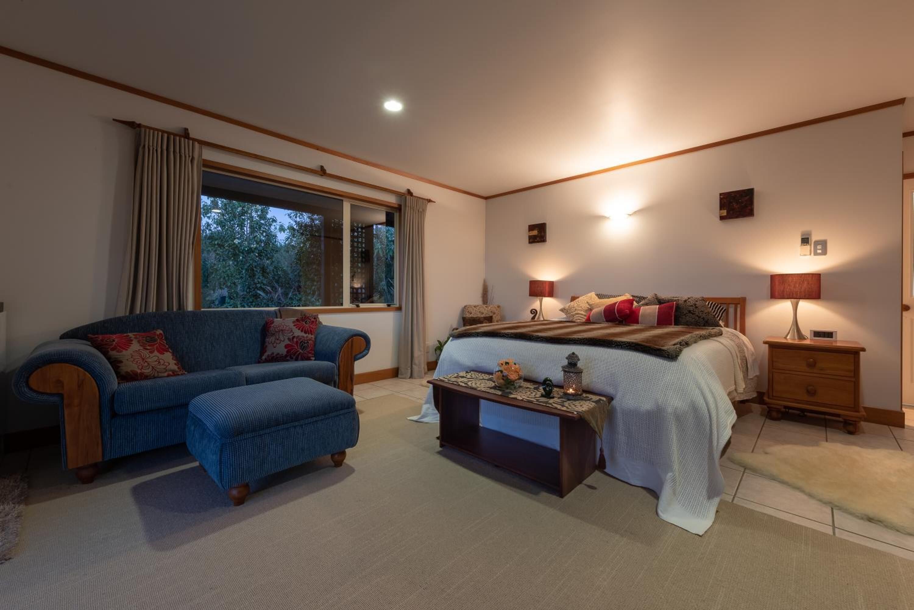 A bedroom with a bed, a sofa, a nightstand, and a window with curtains.