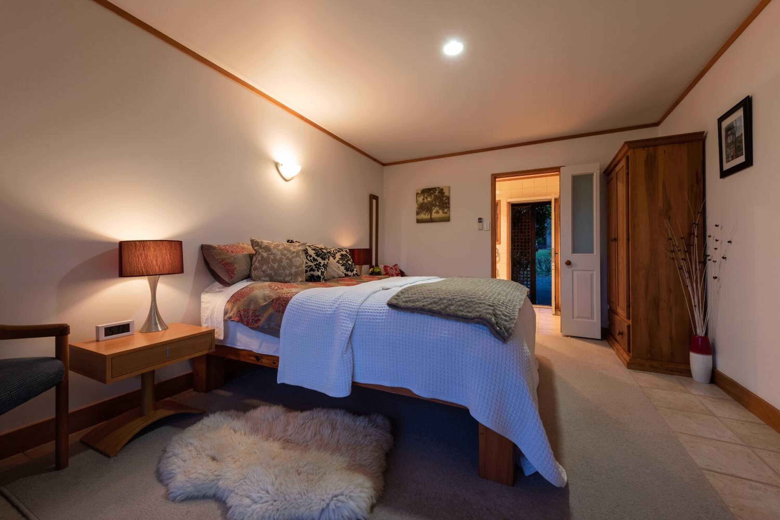 A bedroom with a bed, bedside table, lamp, and a fur rug.