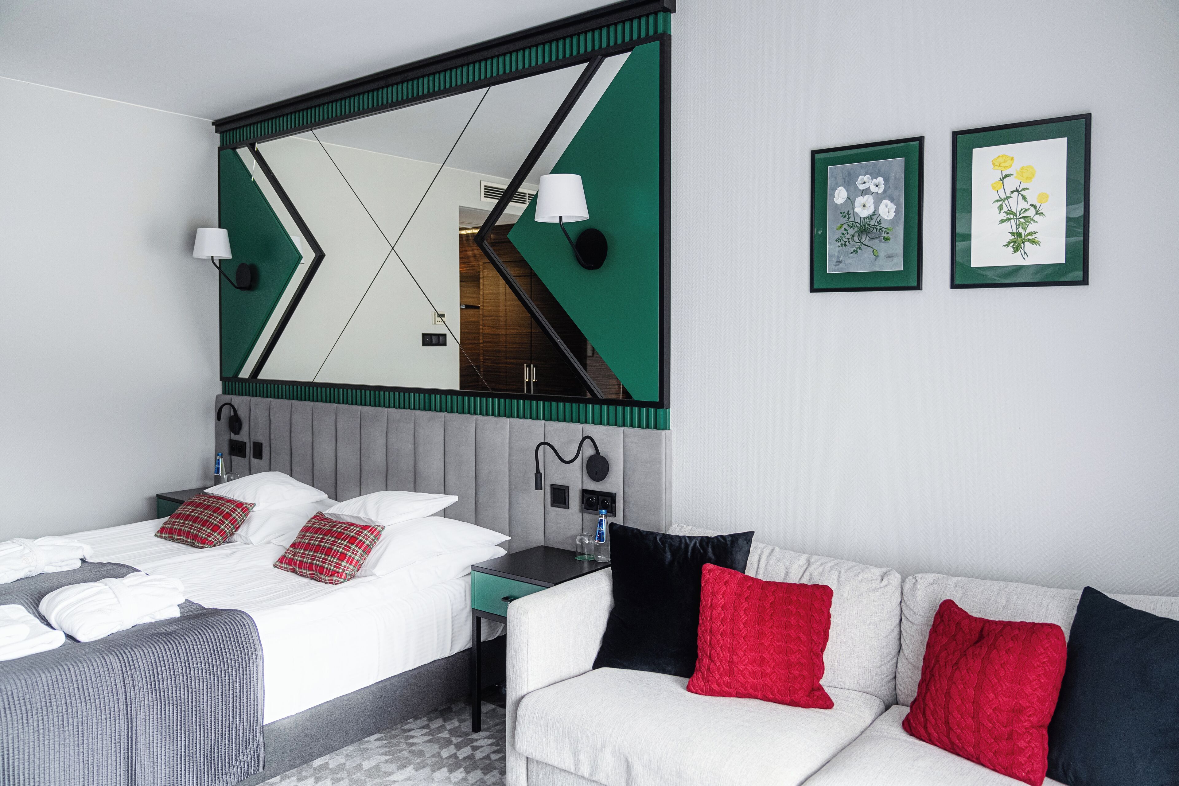 Una moderna camera d'albergo con un letto grande, un divano, una scrivania e uno specchio con motivi geometrici.