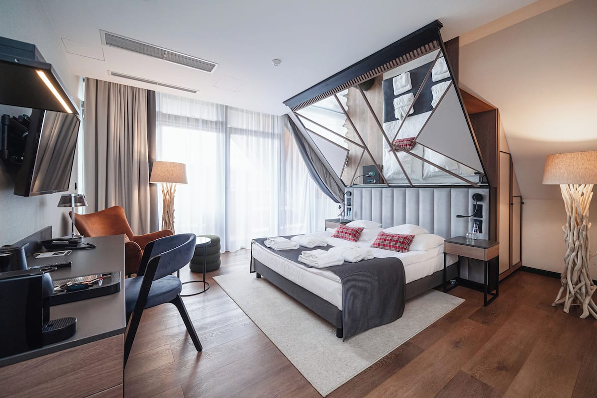 A modern hotel room with a bed, desk, chair, and a large mirror.