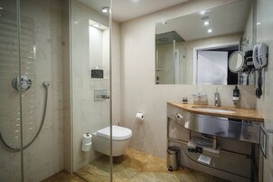 Un baño moderno con ducha de vidrio, inodoro, lavamanos con tocador y un espejo grande.