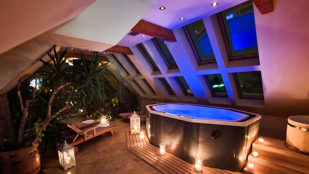 A hot tub in a covered outdoor area with wooden flooring, surrounded by potted plants and candles.