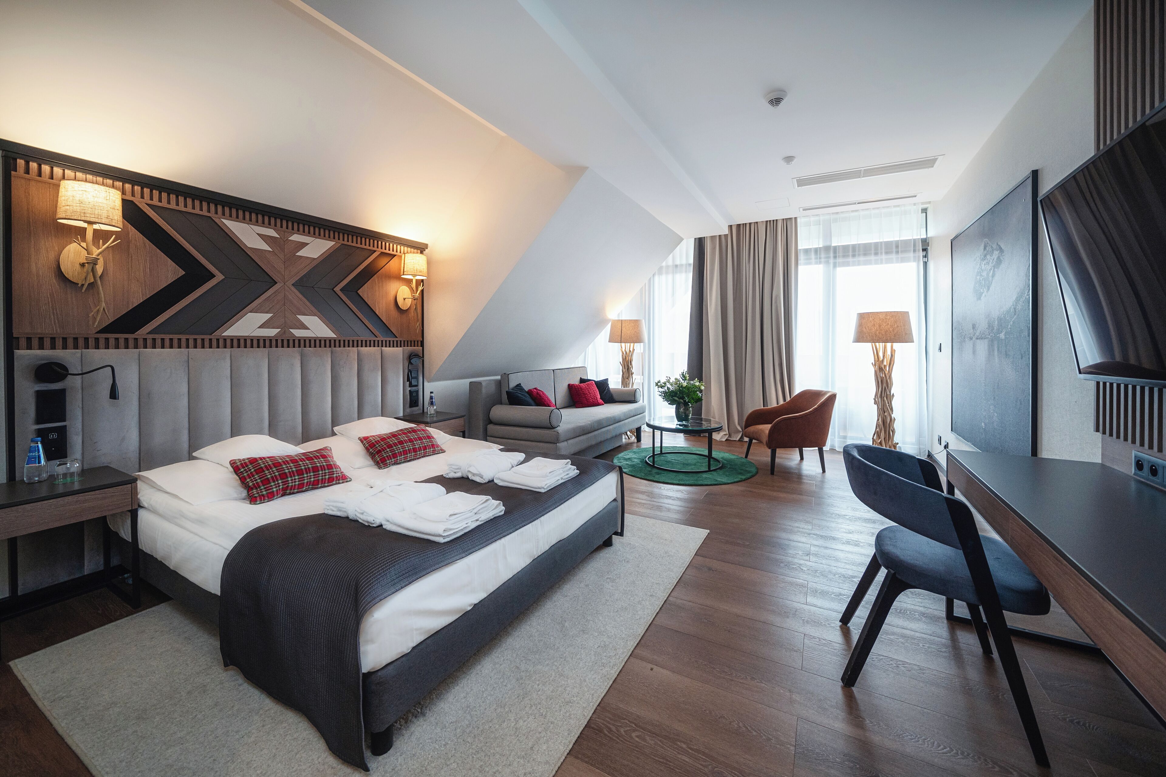 A modern hotel room with a large bed, a desk, a chair, and a TV.