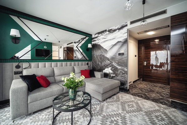 A modern living room with a grey sectional sofa, a glass coffee table, and a large mirror.