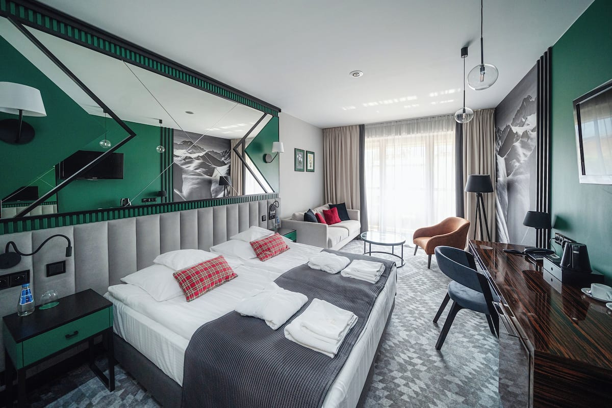 A modern hotel room with a large bed, a desk, a chair, a TV, and a mirror.