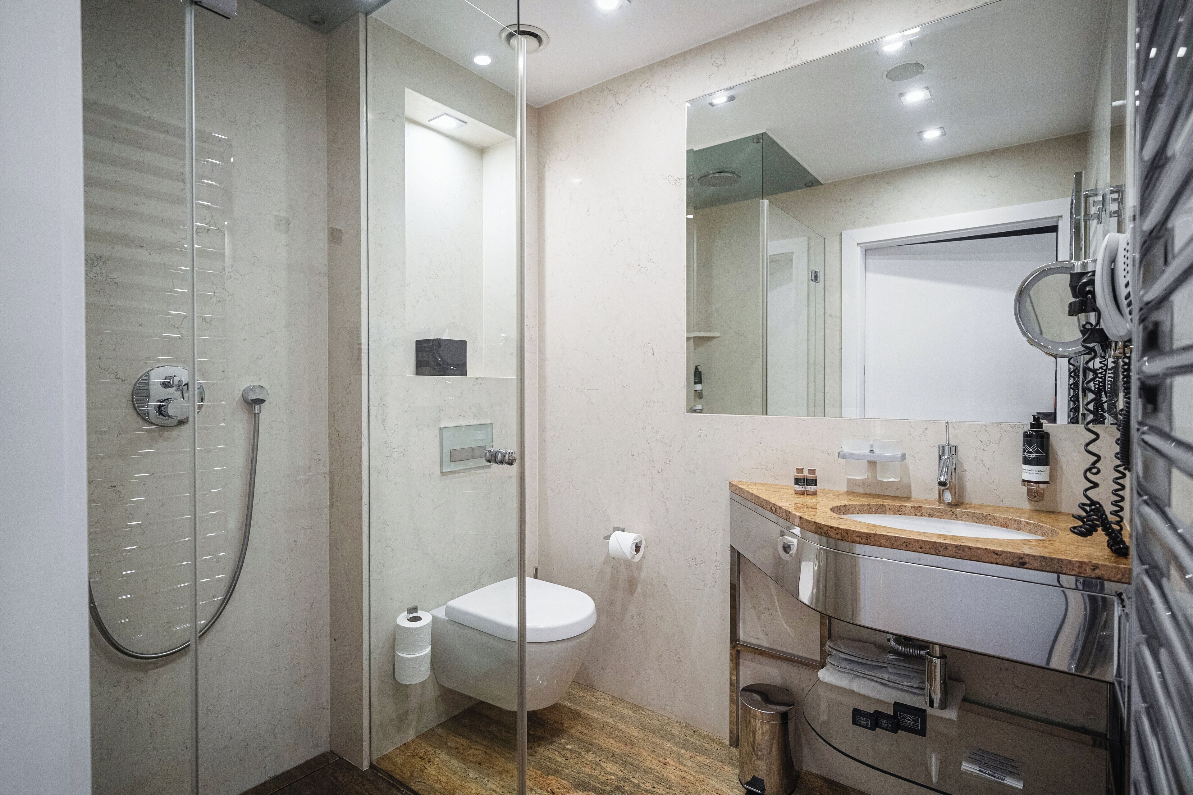 A modern bathroom with a glass-enclosed shower, a toilet, a sink with a mirror, and a trash bin.