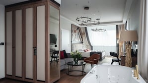 A modern hotel room with a large bathtub, a sofa, a dining table, and a TV.