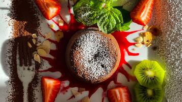 A dessert plate with a chocolate cake, strawberries, kiwi slices, mint leaves, and a scoop of pink ice cream.