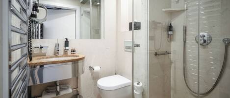 Un baño moderno con ducha envuelta en vidrio, inodoro y tocador con espejo y lavamanos.