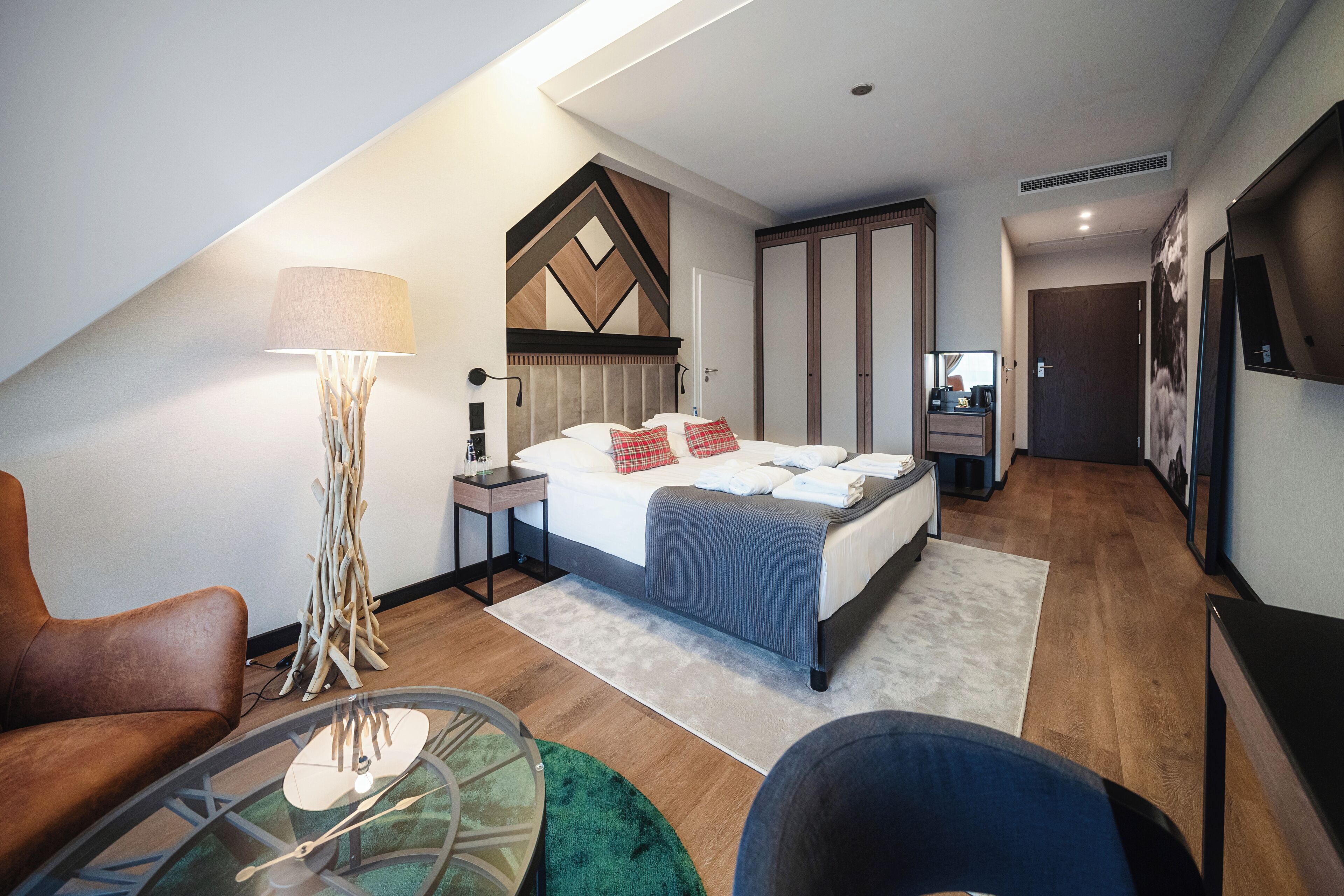 Une chambre d’hôtel moderne équipée d’un lit, d’un bureau, d’une chaise, d’une lampe et d’une horloge murale.