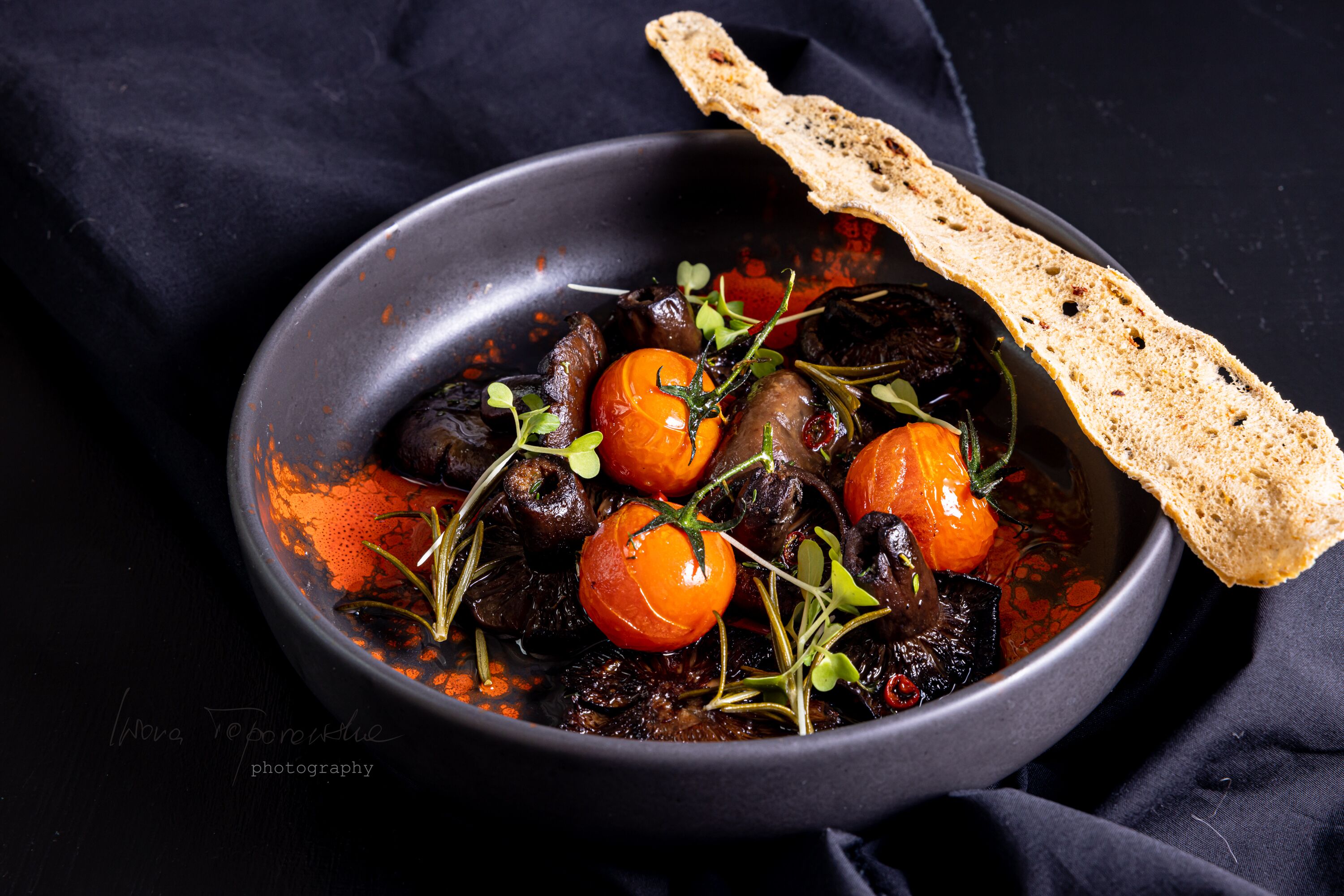 A bowl of food with bread on a dark cloth.